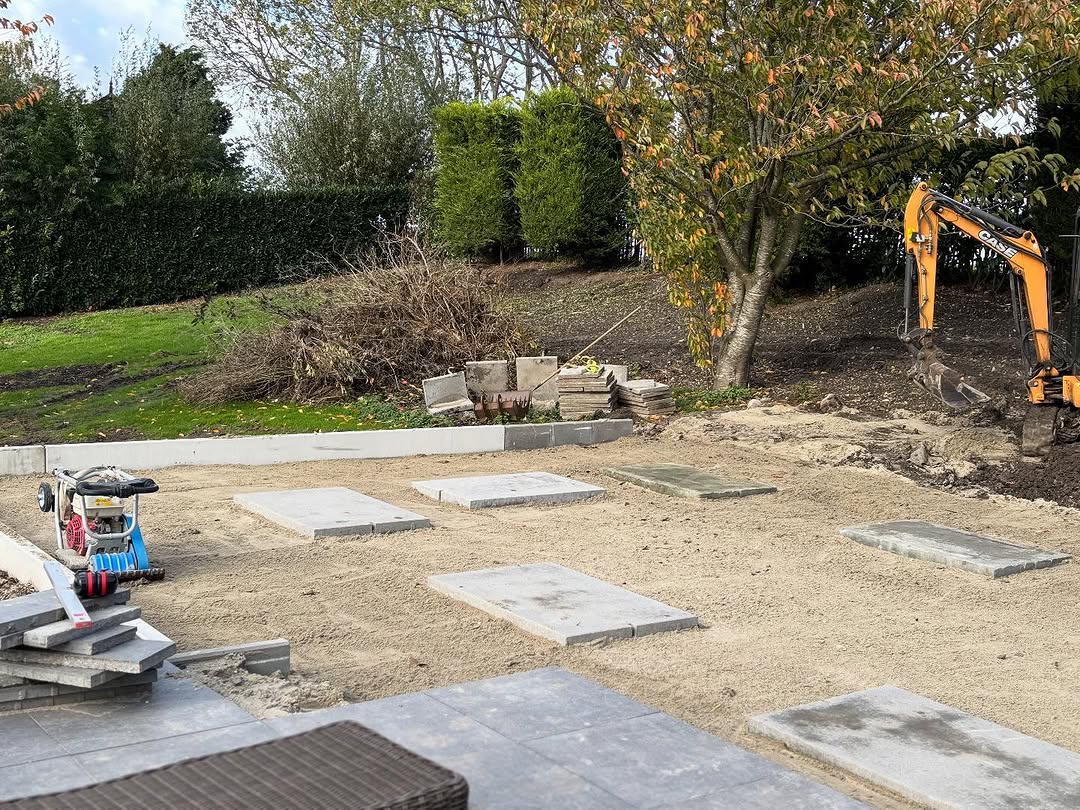 Aanleg fundatie voor een mantelzorgwoning, tegels op zand met machine op de achtergrond