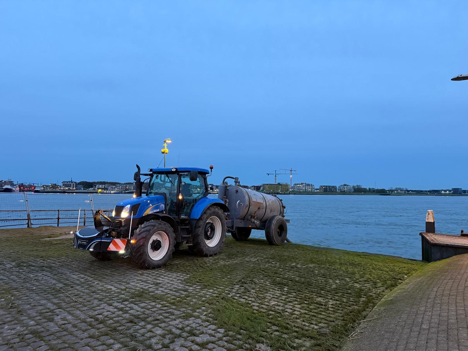 Tractor op de dijk langs de rivier in de avond