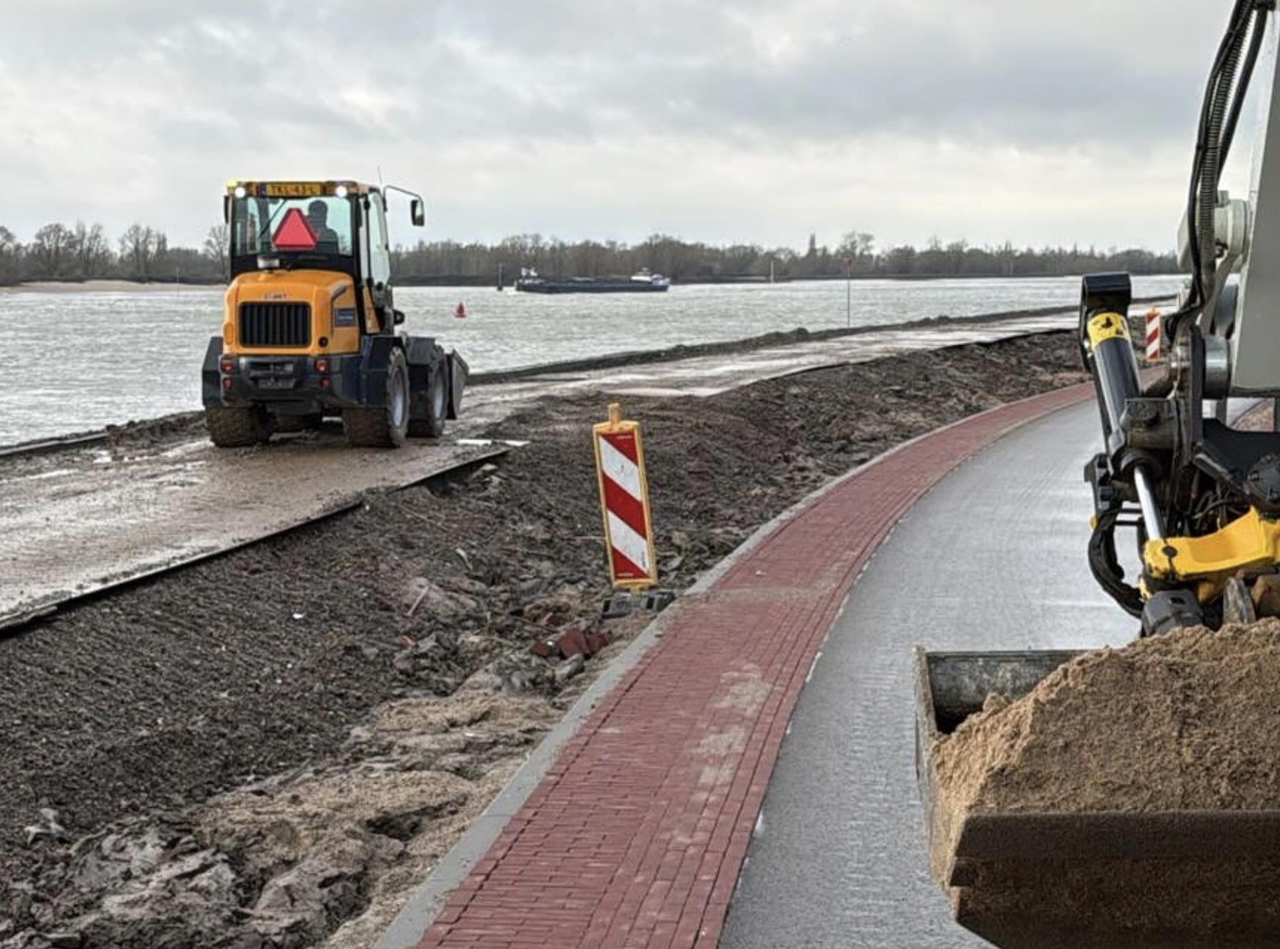 Werkzaamheden langs de rivier met passerend schip