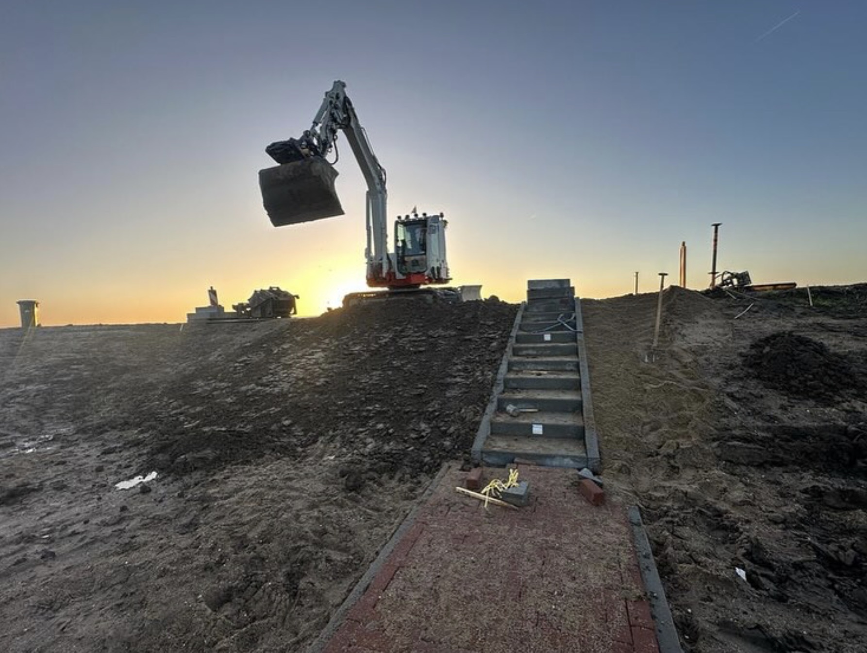 Graafmachine bij zonsondergang op dijktrace